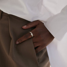 Load image into Gallery viewer, View of black woman&#39;s hand halfway in trouser pocket allowing Silver pearl ring to be visible on index finger. Wearing a white shirt and brown trousers