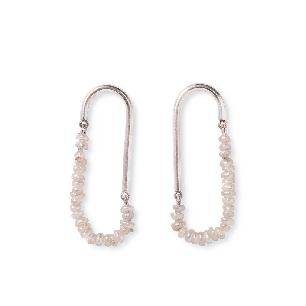Silver pearl earrings laying flat on white surface. The earrings are made from silver canes with small hoops on both ends of each cane to attach a string of tiny pearls in a loose loop.